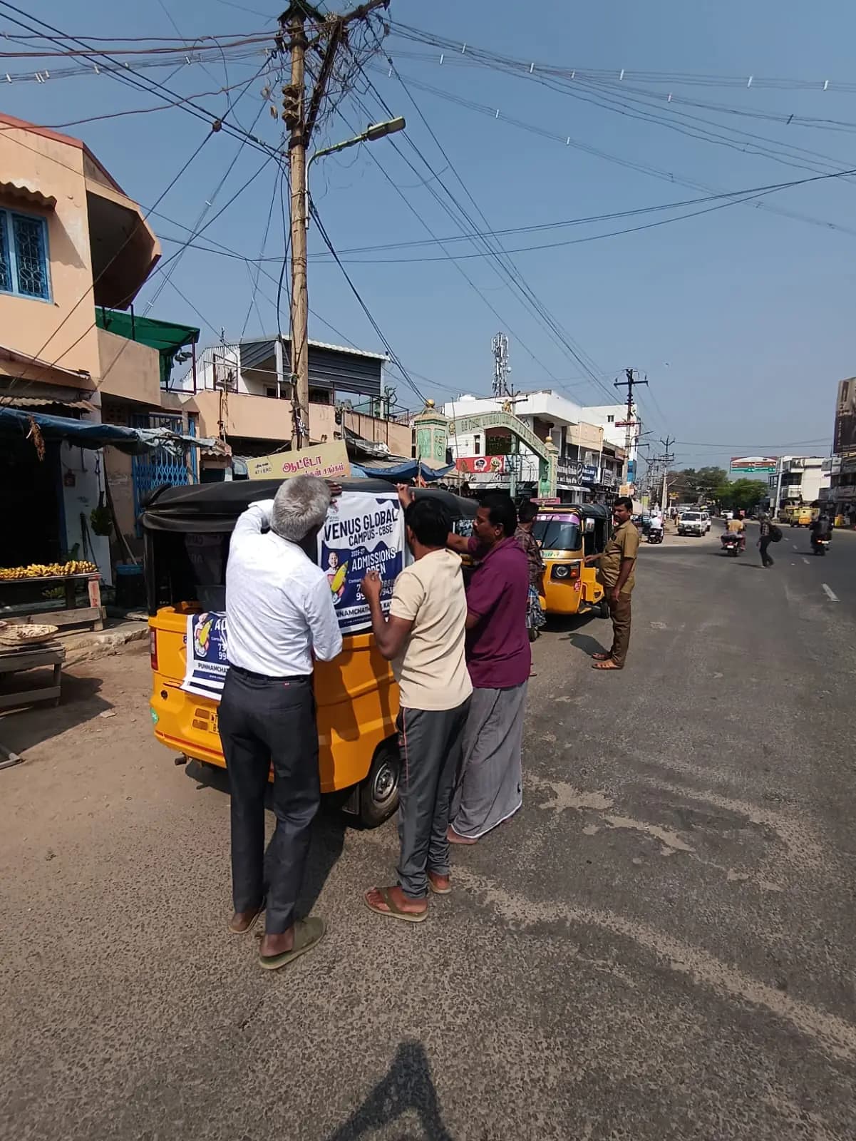 Team fixing auto-rickshaw back-panel ad on street