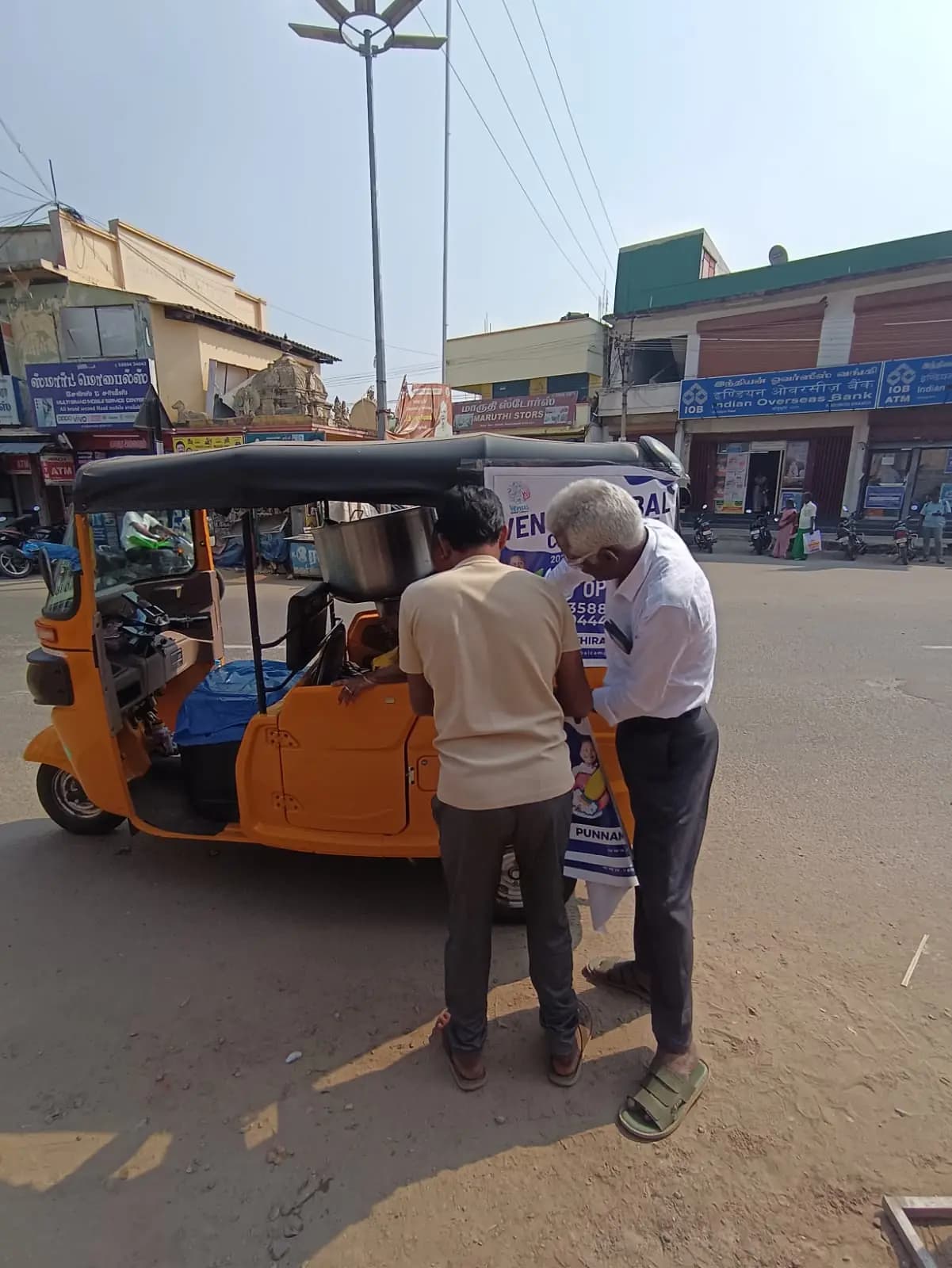 Team fixing auto-rickshaw back-panel ad on street